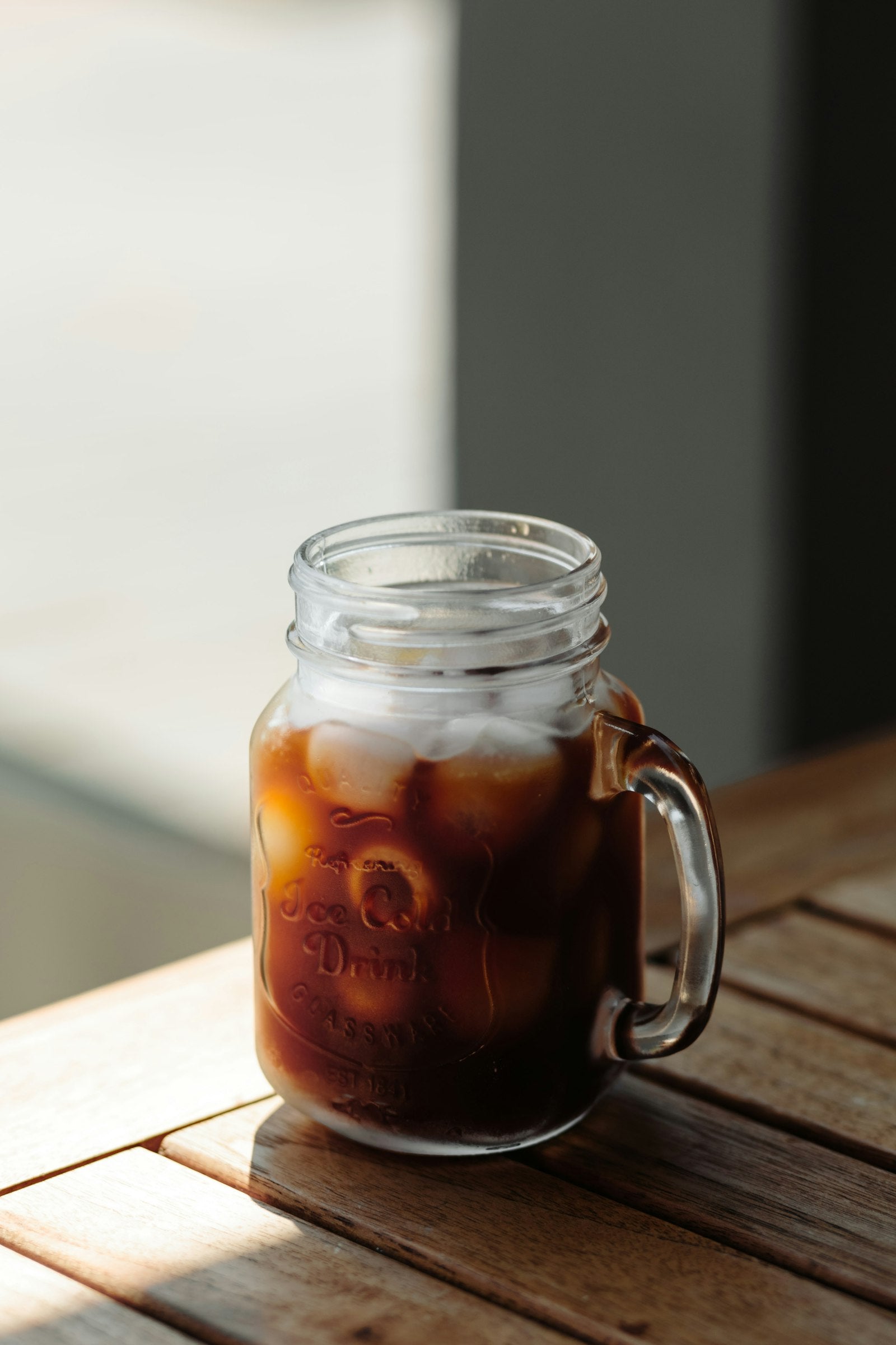 Cold brew coffee over ice in a mason jar mug on a wooden table